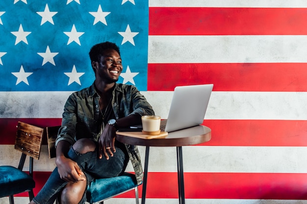 Porträt eines glücklichen afrikanischen Geschäftsmannes, der in einem Café sitzt und am Laptop arbeitet, eine Kaffeepause einlegen.