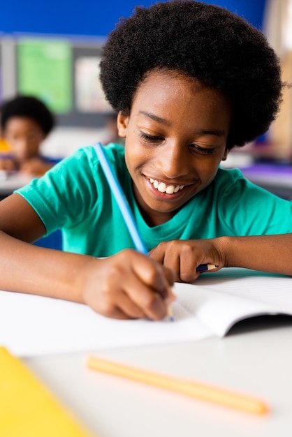 Porträt eines glücklichen afroamerikanischen Grundschülers, der im Schreibtisch im Klassenzimmer schreibt