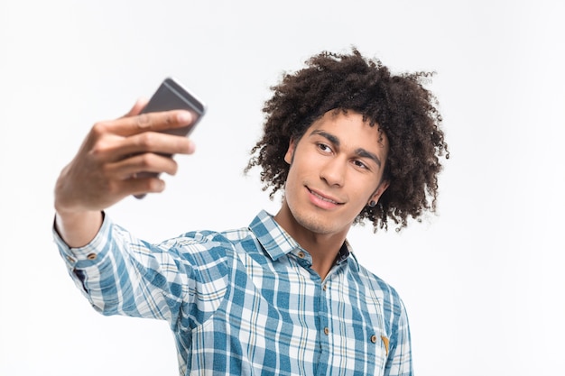 Porträt eines glücklichen afroamerikanischen Mannes, der ein Selfie-Foto auf dem Smartphone macht, isoliert auf einer weißen Wand