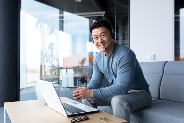 Porträt eines glücklichen asiatischen Call-Center-Mitarbeiters, der lächelt und glücklich mit Headset und Computer-Videoanruf-Online-Hilfe für Remote-Arbeit arbeitet