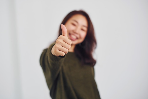 Porträt eines glücklichen asiatischen jungen Mädchens, das im Studio vor weißem Hintergrund den Daumen nach oben zeigt.