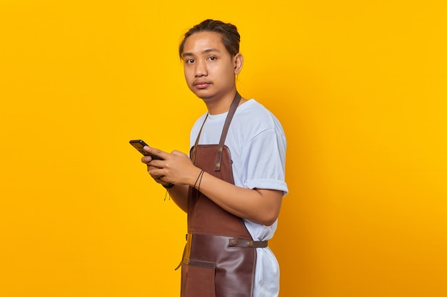 Porträt eines glücklichen asiatischen jungen Mannes mit Smartphone und Blick auf die Vorderseite auf gelbem Hintergrund