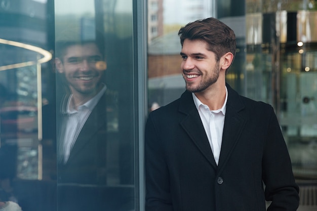 Porträt eines glücklichen Geschäftsmannes, der in der Nähe des Geschäftszentrums steht und beiseite schaut.