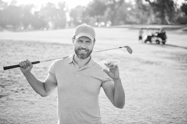 Foto porträt eines glücklichen golfspielers in mütze mit golfschläger, der ballgolf zeigt