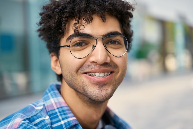 porträt eines glücklichen, gutaussehenden, erfolgreichen studenten, der eine brille trägt und in der nähe des college sitzt und lächelt