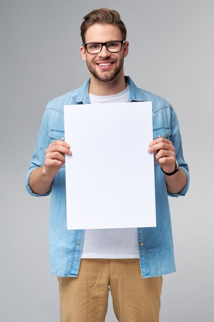 Porträt eines glücklichen gutaussehenden jungen Mannes, der leere weiße Karte oder Zeichen hält