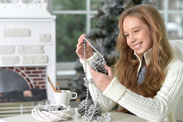 Porträt eines glücklichen jugendlich Mädchens mit Weihnachtsdekorationen, die zu Hause am Tisch sitzen