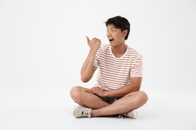 Porträt eines glücklichen jungen asiatischen Mannes, der mit gekreuzten Beinen sitzt