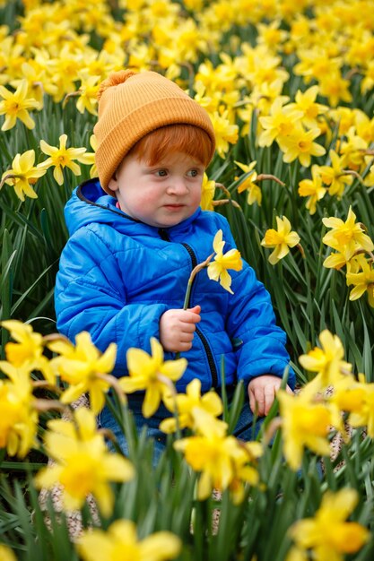 Foto porträt eines glücklichen jungen, der die ostereierjagd auf einem feld mit gelben narzissen genießt