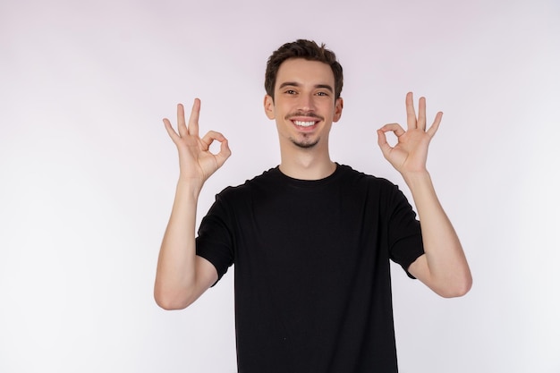 Porträt eines glücklichen jungen gutaussehenden Mannes, der mit der Hand und den Fingern auf weißem Hintergrund ein Ok-Zeichen tut