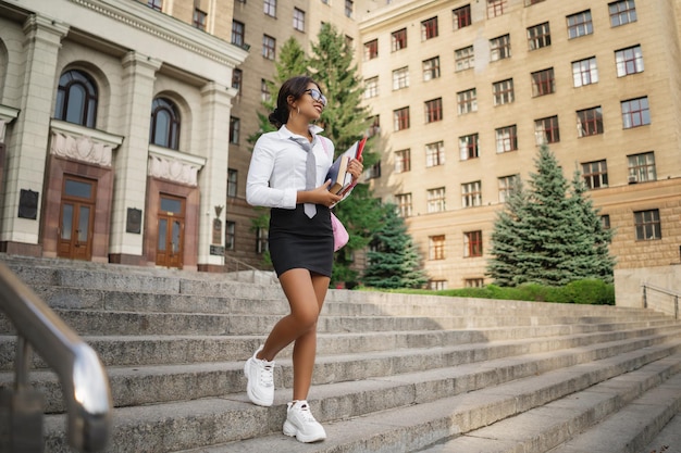 Porträt eines glücklichen jungen Mädchens mit Büchern, die auf der Stadttreppe stehen