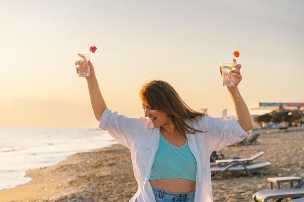 Porträt eines glücklichen jungen Mädchens mit einem Cocktail in der Hand auf einem Hintergrund des schönen Meeres Mädchen, das Spaß im Sommerurlaub hat Freiheit und Glück