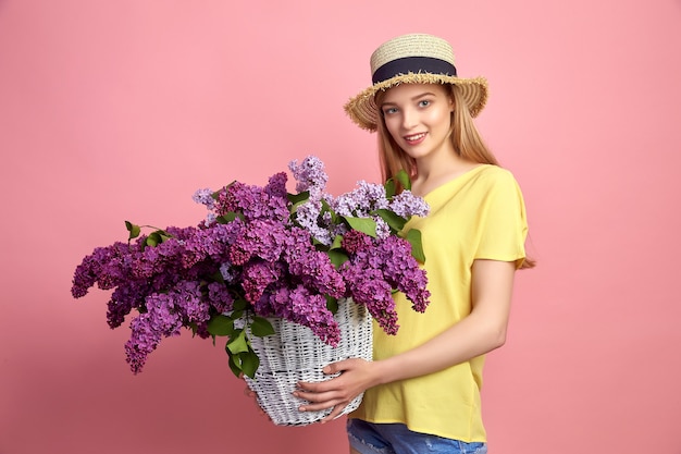 Porträt eines glücklichen jungen Mädchens mit Korb voller Flieder auf rosa Hintergrund.