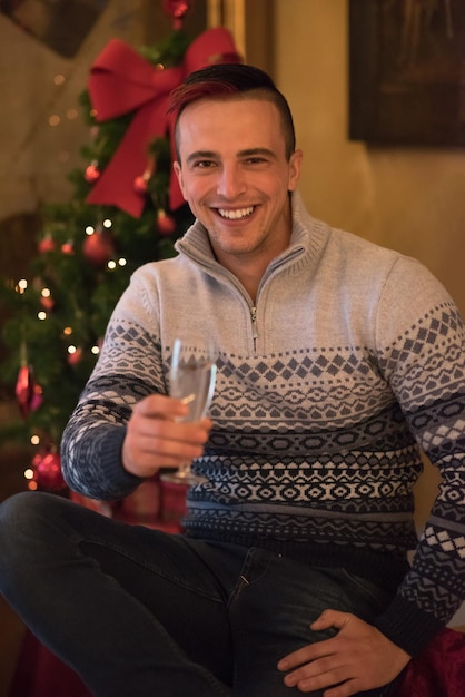 Porträt eines glücklichen jungen Mannes mit einem Glas Champagner, der die Winterferien zu Hause feiert, schön dekoriert für Weihnachten