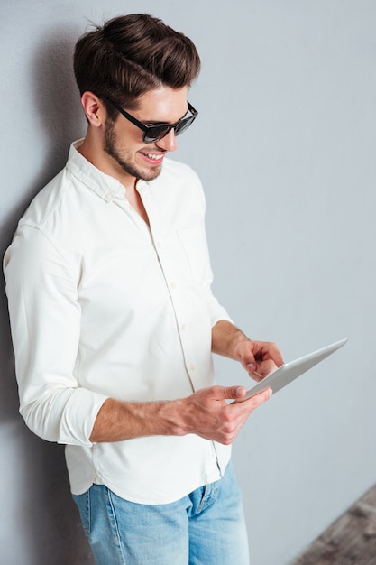 Foto porträt eines glücklichen jungen mannes mit sonnenbrille mit tablet-computer isoliert