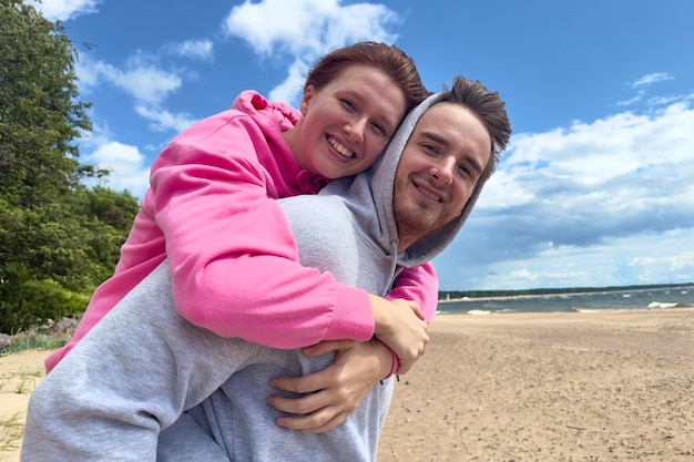 Porträt eines glücklichen jungen Paares, das am Strand spaziert und sich liebevoll umarmt. Der Mann trägt seine Freundin