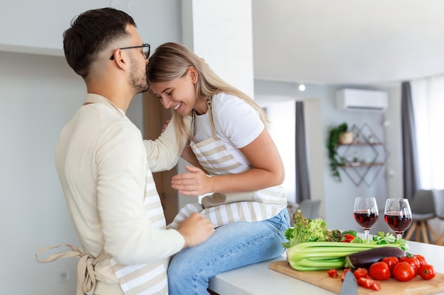 Porträt eines glücklichen jungen Paares, das zu Hause zusammen in der Küche kocht. Attraktive junge Frau und ein gutaussehender Mann genießen es, Zeit miteinander zu verbringen, während sie auf einer hellen, modernen Küche stehen