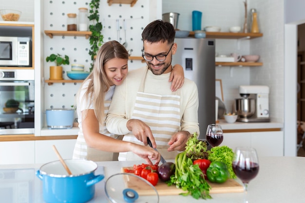 Porträt eines glücklichen jungen Paares, das zu Hause zusammen in der Küche kocht. Attraktive junge Frau und ein gutaussehender Mann genießen es, Zeit miteinander zu verbringen, während sie auf einer hellen, modernen Küche stehen