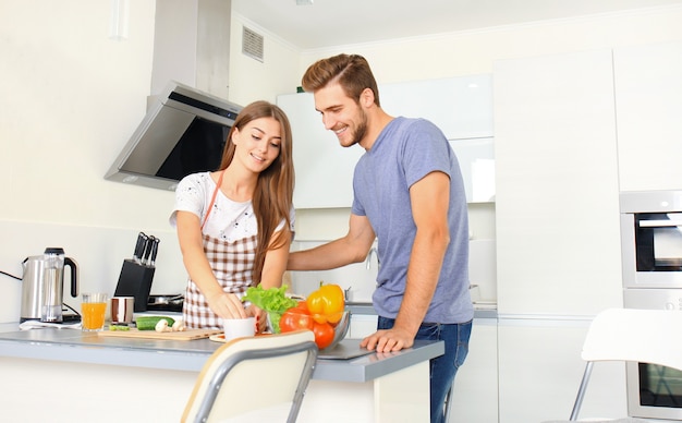 Porträt eines glücklichen jungen Paares, das zu Hause zusammen in der Küche kocht.