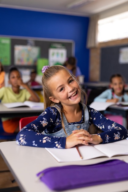 Porträt eines glücklichen kaukasischen Schulmädchens in einer vielfältigen Grundschulklasse