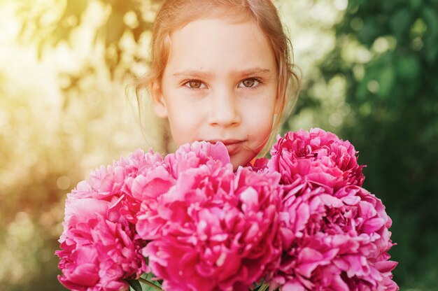 Porträt eines glücklichen kleinen kaukasischen siebenjährigen Mädchens, hält einen Strauß rosa Pfingstrose in den Händen