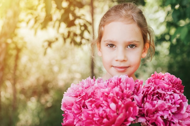 Porträt eines glücklichen kleinen kaukasischen siebenjährigen Mädchens, hält einen Strauß rosa Pfingstrose in den Händen