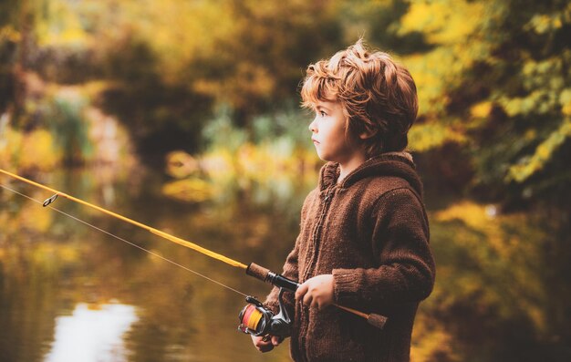 Porträt eines glücklichen kleinen Sohnes, der mit Spinnrolle auf dem Fluss fischt glückliche Kinder Herbstwochenende con