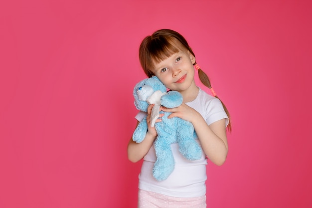 Porträt eines glücklichen Mädchens 5-6 Jahre alt auf einer rosa Wand mit einem Teddybär in ihren Händen, bereitet sich das Kind auf das Bett vor