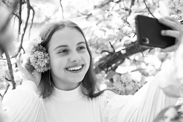 Porträt eines glücklichen Mädchens, das im Frühling ein Selfie mit dem Smartphone am blühenden Sakura-Kirschbaum macht