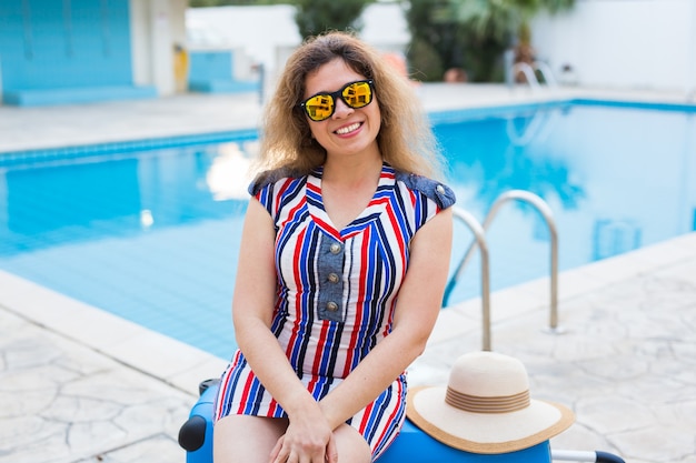 Porträt eines glücklichen Mädchens in den Sommerferien gegen Pool, gestreiftes Kleid und Sonnenbrille.