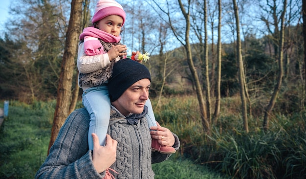 Porträt eines glücklichen Mannes, der kleinem Mädchen in den Wald huckepack fährt