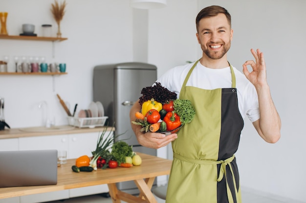 Porträt eines glücklichen Mannes, der zu Hause einen Teller mit frischem Gemüse auf dem Hintergrund der Küche hält