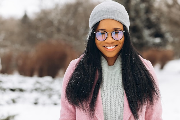 Porträt eines glücklichen positiven Mädchens Afroamerikanische junge Frau mit Brille und Handschuhen im Winterpark