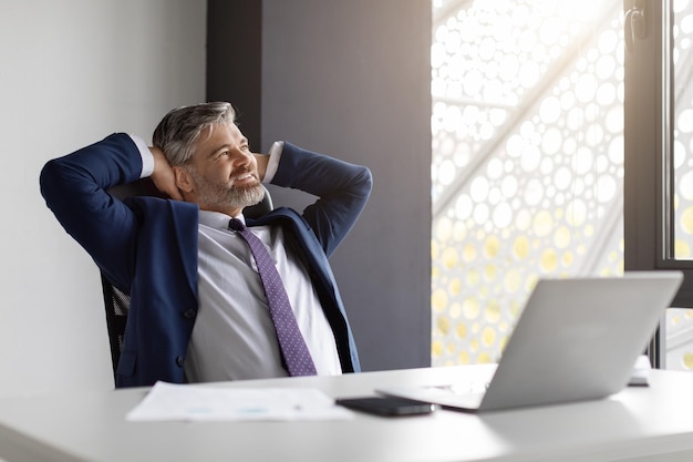 Porträt eines glücklichen reifen männlichen Unternehmers, der sich am Arbeitsplatz im Büro entspannt