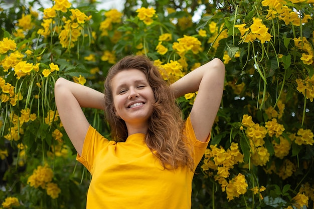 Porträt eines glücklichen, schönen bärtigen Mädchens, junge positive Frau mit Bart riecht schöne gelbe Blumen im Garten, lächelt und genießt den Frühlings- oder Sommertag, der tief tief frische Luft atmet