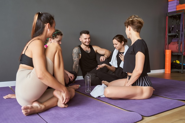 Porträt eines glücklichen, schönen Teams, das auf den lila Matten sitzt, während es sich im Fitness-Yoga-Kurs unterhält?