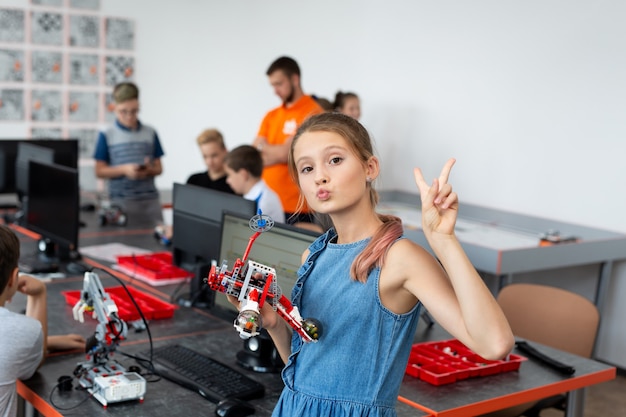 Porträt eines glücklichen Schulmädchens in einer Robotikklasse, sie hält einen Roboter, der aus den auf einem Computer programmierten Kunststoffteilen zusammengesetzt ist