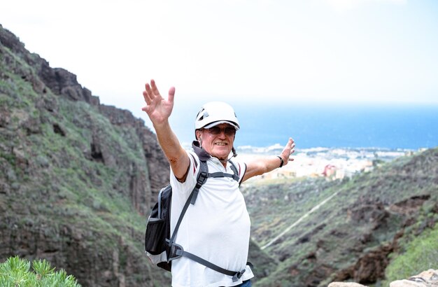 Porträt eines glücklichen Senioren-Wanderers mit Helm auf dem Gipfel des Berges Lächelnder Klettertourist