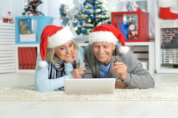 Porträt eines glücklichen Seniorenpaares, das zu Hause Weihnachten mit Laptop auf dem Boden liegt