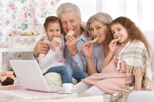 Porträt eines glücklichen Seniorenpaares mit Enkelkindern und Laptop zu Hause