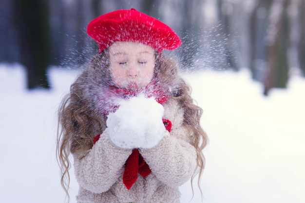 Porträt eines glücklichen, süßen kleinen blonden Mädchens, das an verschneiten Wintertagen im Freien spaziert und mit ihm spielt
