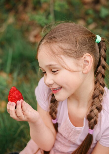 Porträt eines glücklichen süßen kleinen Mädchens isst Erdbeeren am Sommertag Weich fokussierte Vertikale