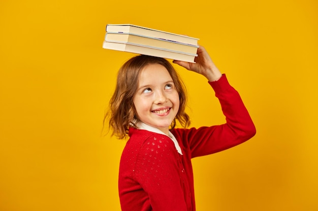 Porträt eines glücklichen Teenager-Schulmädchens in Uniform, das Bücher auf dem Kopf hält