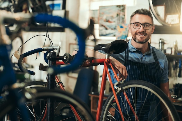 Porträt eines glücklichen und reparierenden Mannes in einer Fahrradwerkstatt für die Arbeit in einer Fahrradwerkstatt und einem Startup. Selbstbewusster Fahrradmechaniker-Kleinunternehmer und reifer männlicher Techniker mit Brille in Australien