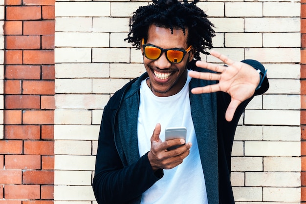 Porträt eines gutaussehenden Afromannes, der sein Handy auf der Straße benutzt.