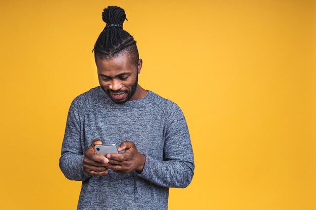 Porträt eines gutaussehenden aufgeregten fröhlichen afroamerikanischen schwarzen Mannes, der beiläufiges Senden und Empfangen von Nachrichten auf gelbem Hintergrund trägt. Telefon verwenden.