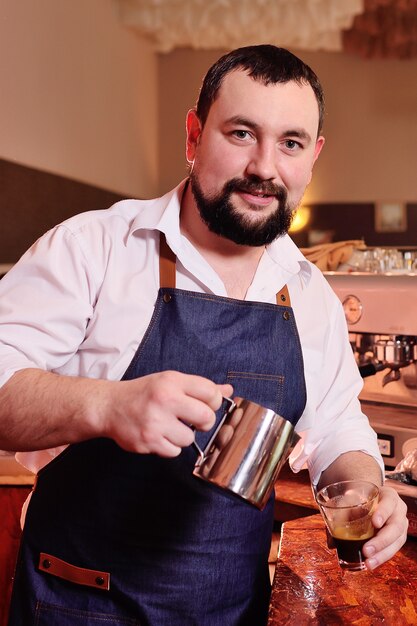 Porträt eines gutaussehenden bärtigen Barista, der Kaffee auf dem Hintergrund eines Cafés und einer Kaffeemaschine zubereitet