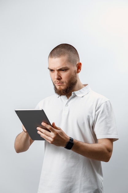 Porträt eines gutaussehenden bärtigen Mannes in einem weißen T-Shirt, das in einer Tablette arbeitet