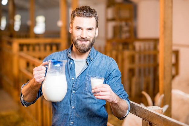 Porträt eines gutaussehenden Bauern mit frischer Milch im Ziegenstall mit Ziegen im Hintergrund. Natürliche Milchproduktion und Landwirtschaft