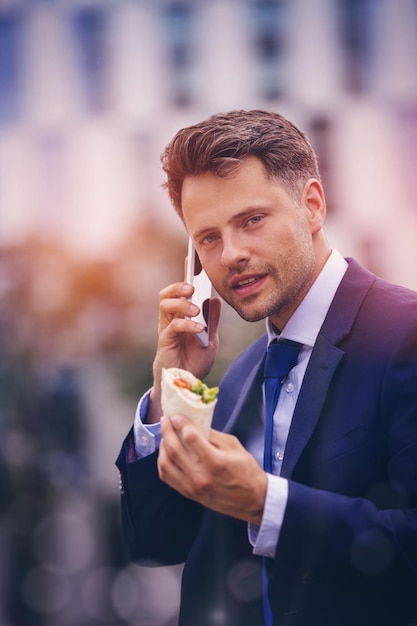 Porträt eines gutaussehenden Geschäftsmannes, der am Handy spricht und Snacks hält